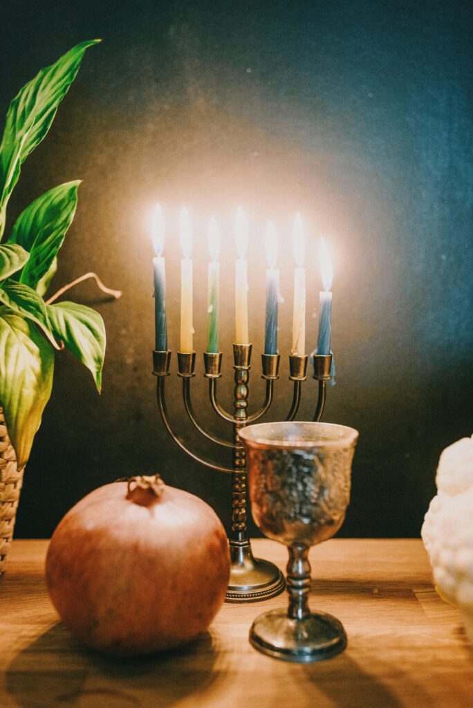 A beautiful menorah lit with candles, accompanied by a pomegranate and a silver chalice, celebrating Hanukkah.